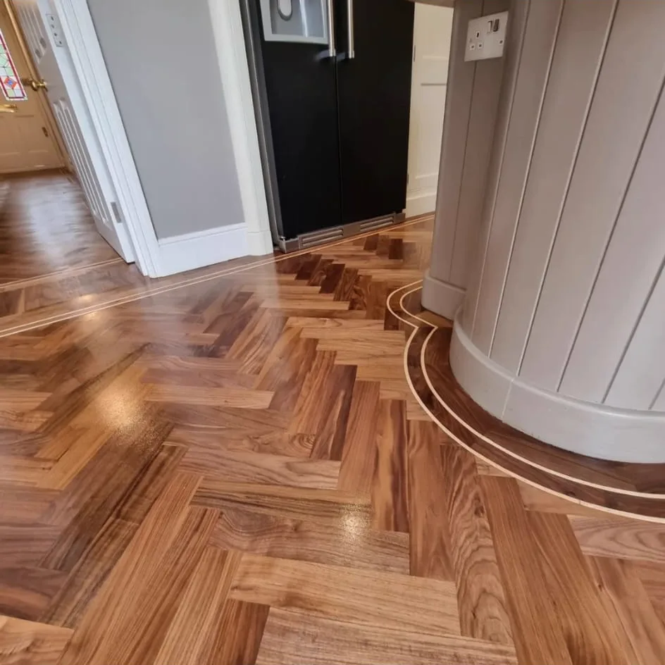 Close-up of the restored double inlay border sweeping around the kitchen island on a Fulham SW6 walnut herringbone floor