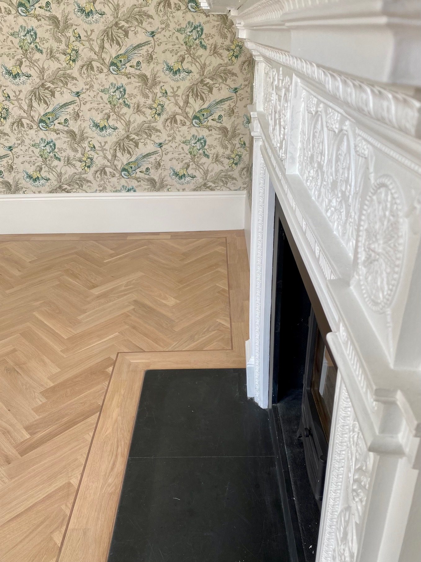 Restored herringbone parquet oak floor beside a period fireplace
