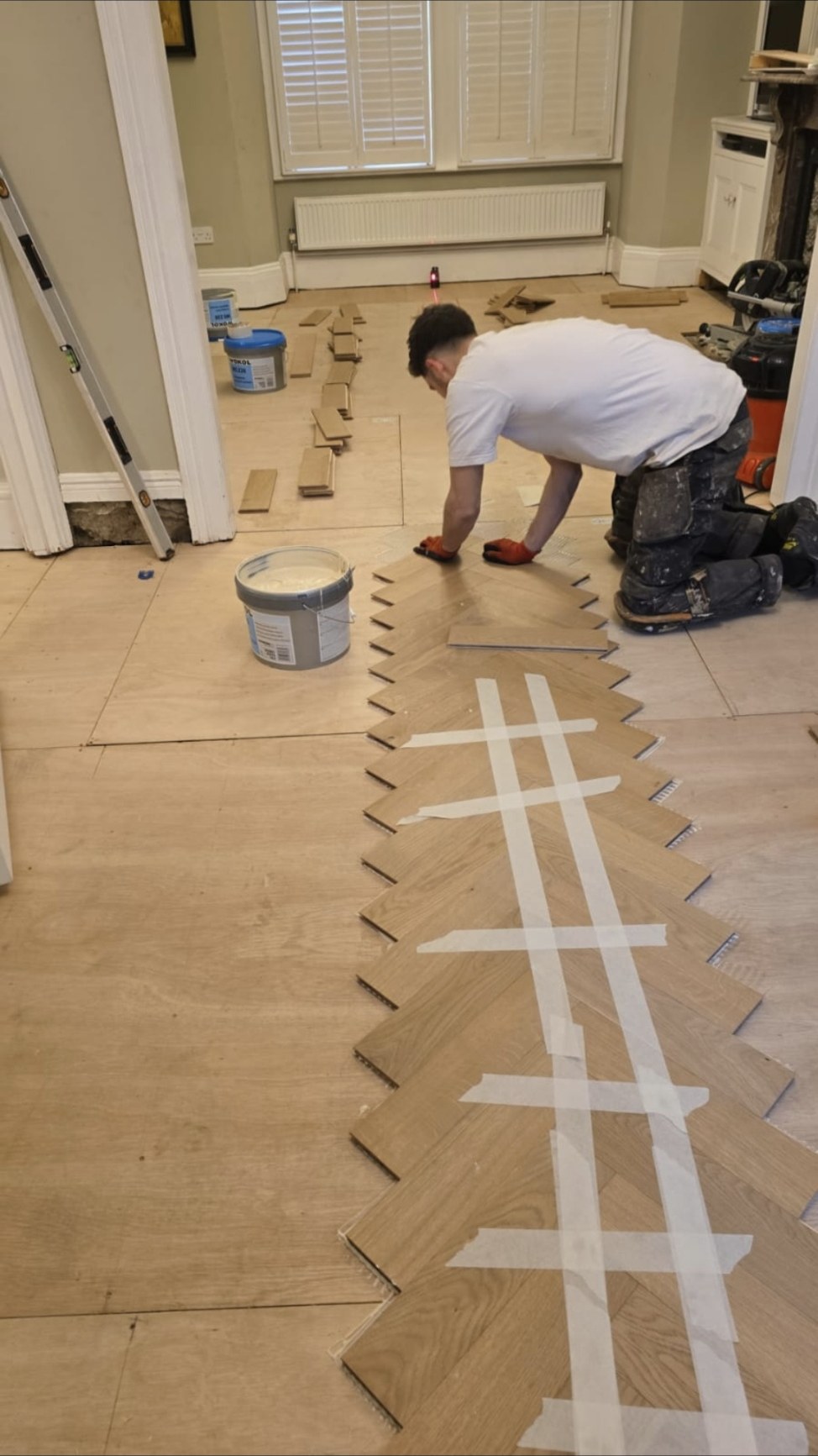 Luke kneeling on a prepared subfloor, laying the centre spine of an oak herringbone floor on a laser line
