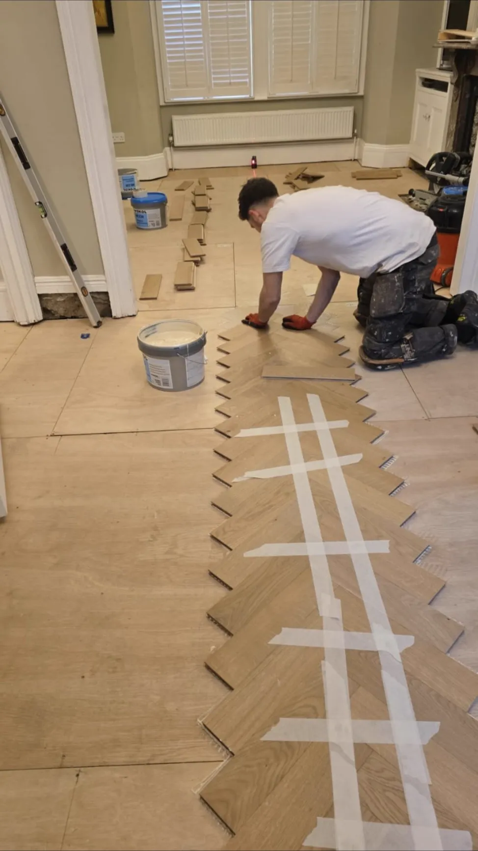 Luke kneeling on a prepared subfloor, laying the centre spine of an oak herringbone floor on a laser line