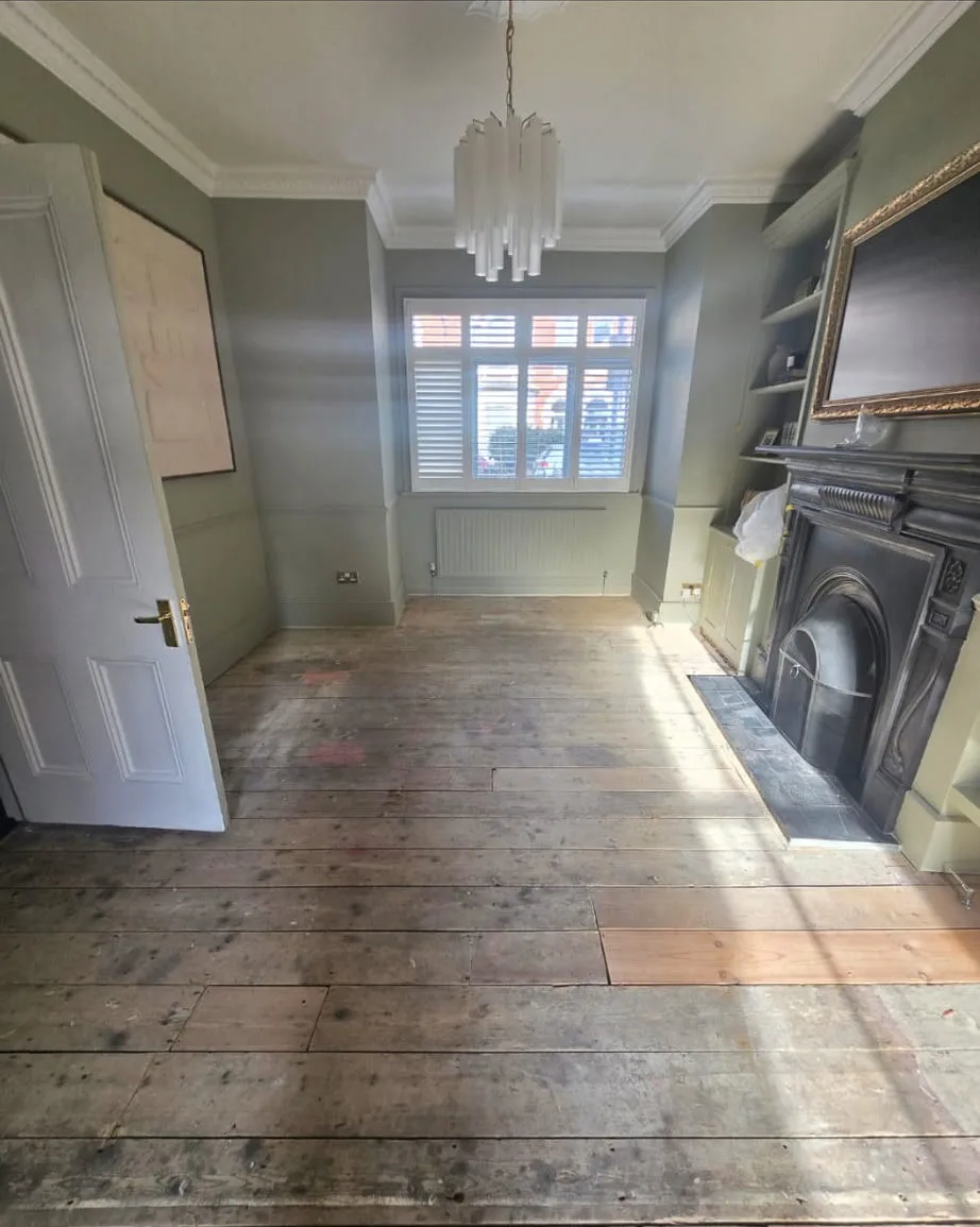 The real room before: bare, worn pine floorboards with patch repairs